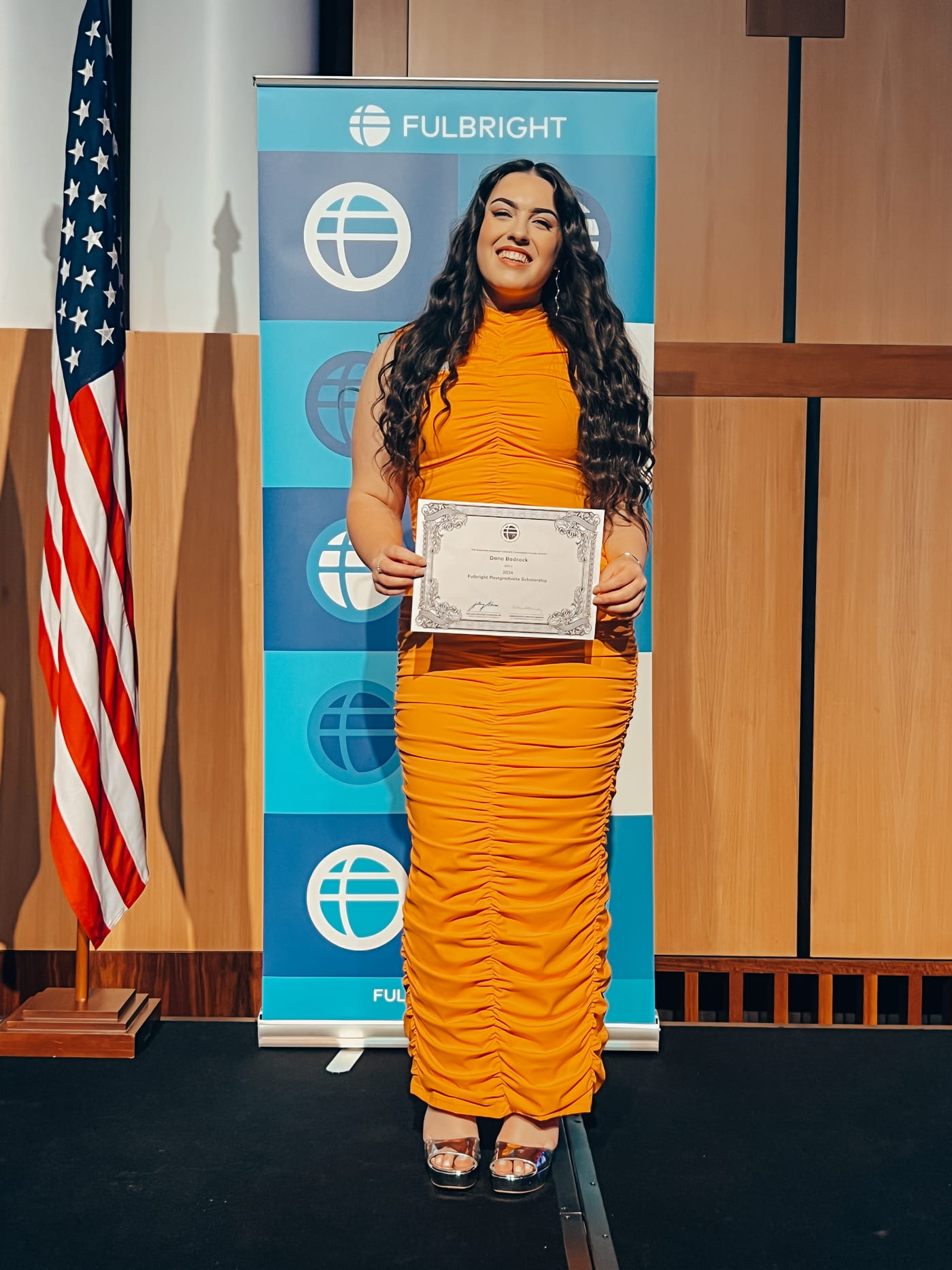 Dana holding her Fulbright certificate beside the United States flag
