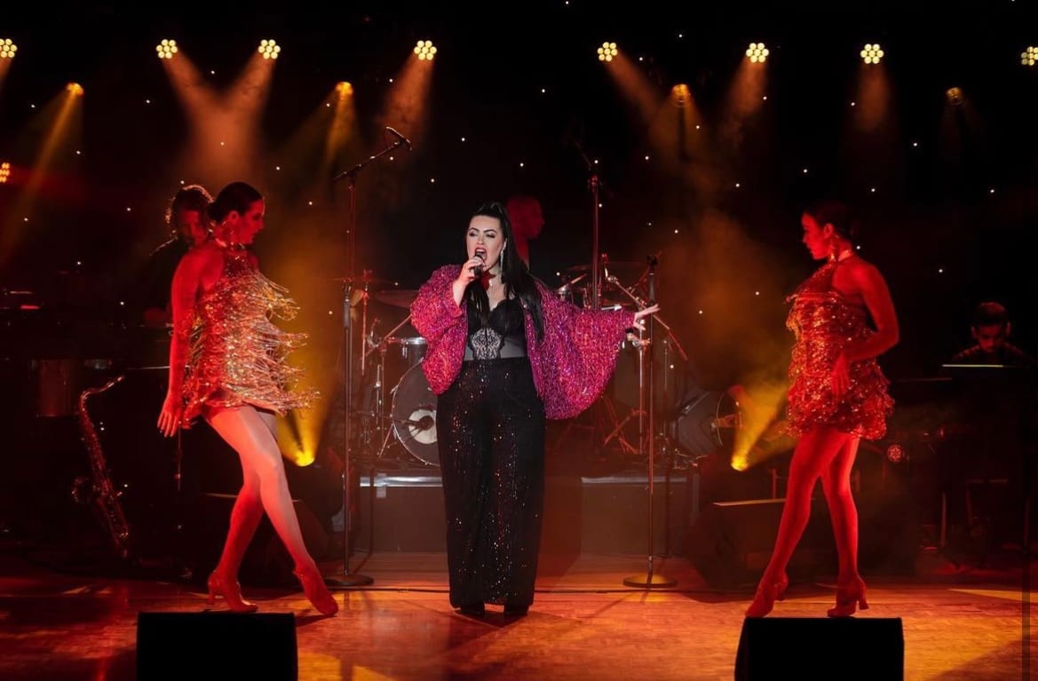 Dana singing centre stage with dancers under stage light
